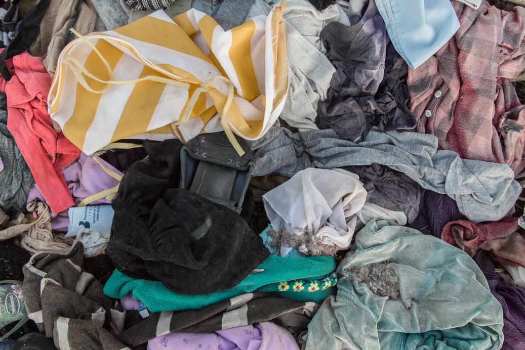 old clothes background, looking down on piles of colourful old clothes discarded on the ground, an informal rubbish dump